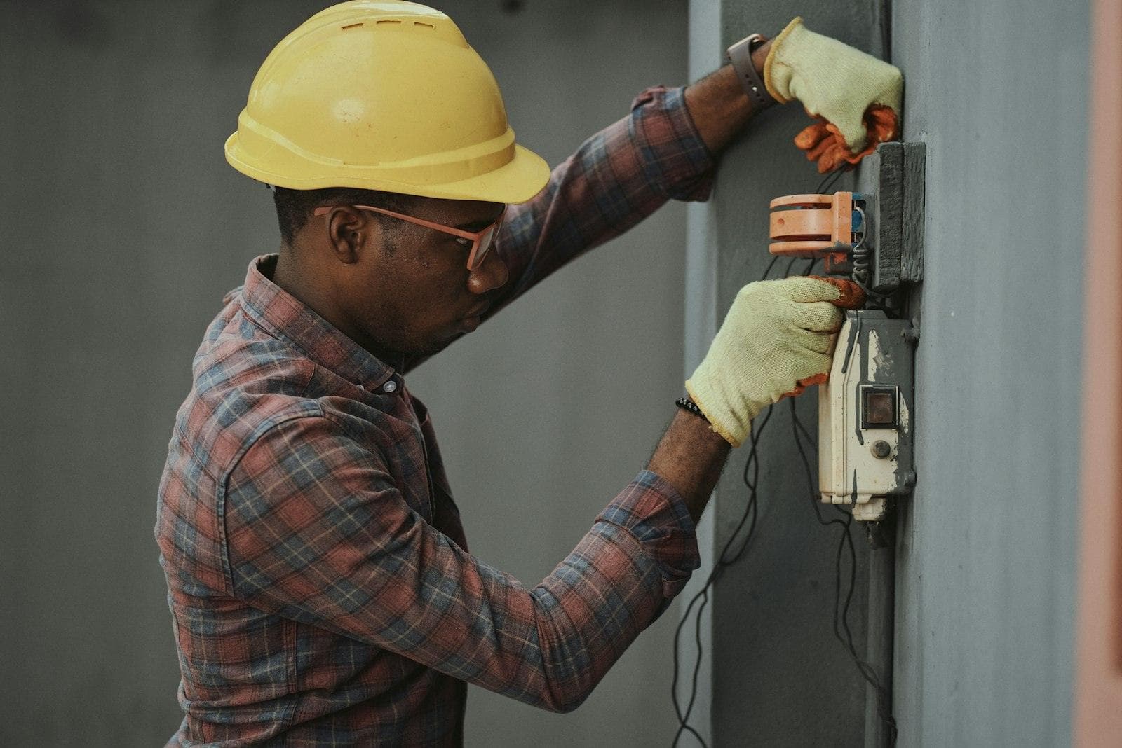 An electrician in a hard hat and gloves working on a meter on site