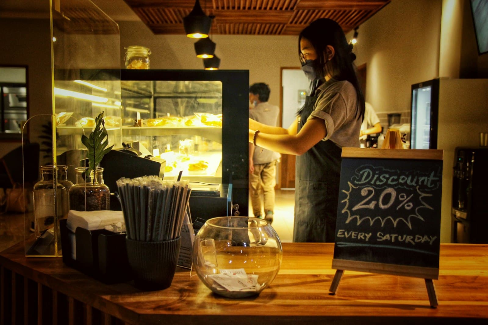 A café counter at closing time, a chalkboard offering 20% off every Saturday beside the pastry case