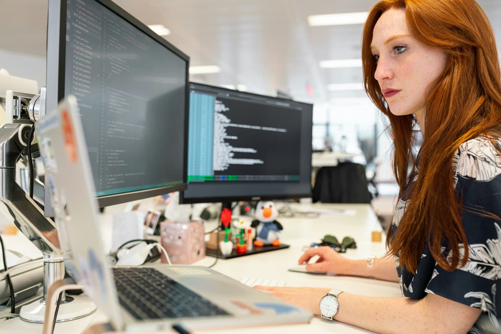 An engineer reading code across two monitors and a laptop in an open office