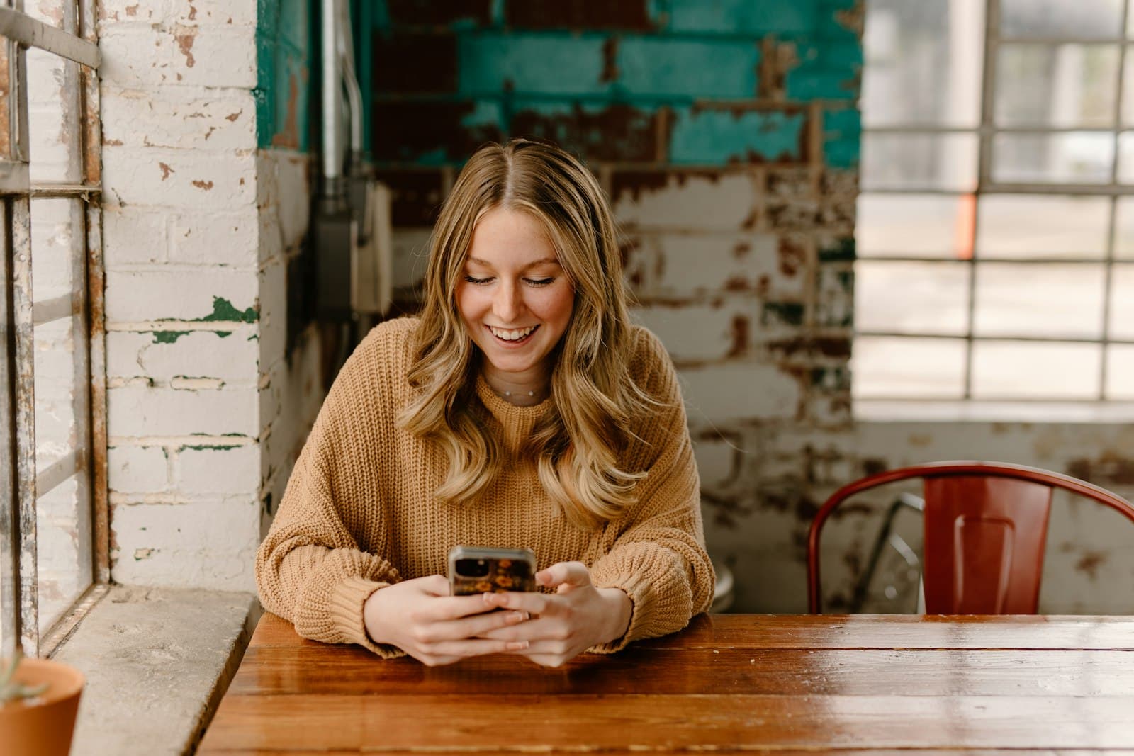 A woman at a café table by the window reading messages on her phone